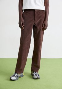 Hnědé kordurové kalhoty s rovný fit, které mají kapsy a jemnou strukturu. Doplnené šedými a žlutými sportovními botami.