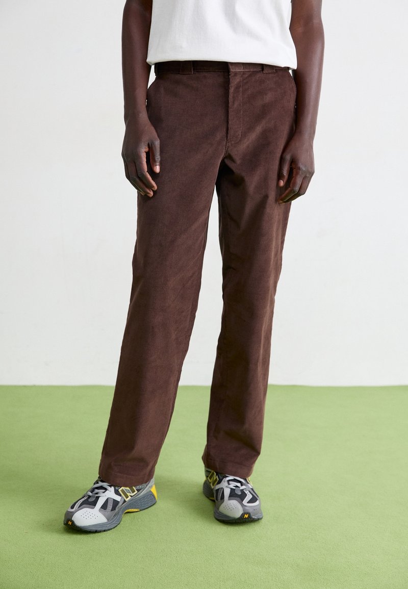 Hnědé kordurové kalhoty s rovný fit, které mají kapsy a jemnou strukturu. Doplnené šedými a žlutými sportovními botami.