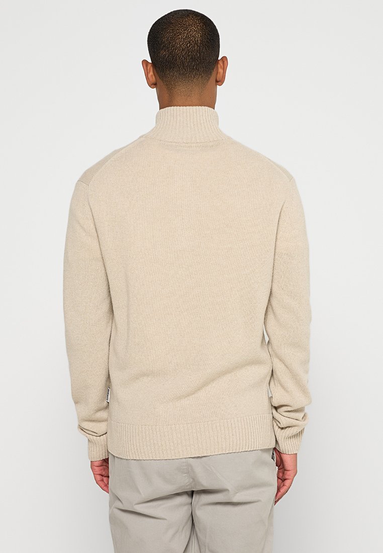Pull en laine beige avec un col montant, des poignets et un ourlet côtelés, et une texture lisse. Le dos présente un design épuré et minimal.