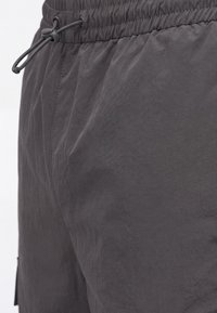 Gros plan sur un short à taille élastique gris foncé avec cordon ajustable et détails de couture visibles.