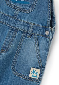 Denim-Overall mit einer hellblauen Waschung, ausgezeichnet mit gestickten Details, mehreren Taschen und einem Etikett mit einem blauen Palmenmuster.