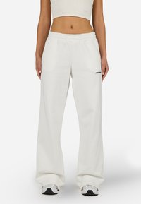 Balti vaļēja piegriezuma sporta bikses ar elastīgu jostu un sānu kabatām. Kreisajā gurnā atrodas melns logo. Mīksts kokvilnas sajaukuma audums.