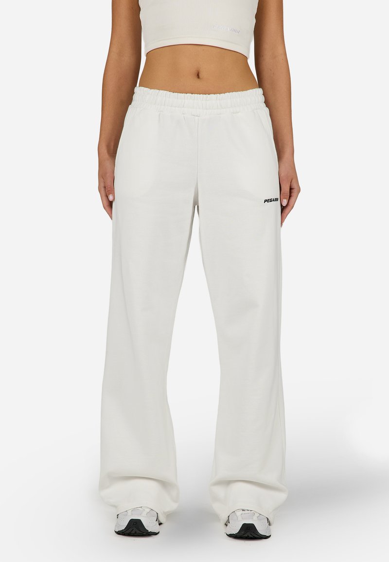 Balti vaļēja piegriezuma sporta bikses ar elastīgu jostu un sānu kabatām. Kreisajā gurnā atrodas melns logo. Mīksts kokvilnas sajaukuma audums.