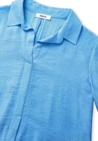 Světle modrá košile s límečkem vyrobená z texturované tkaniny s knoflíkovou légou; má uvolněný střih a měkký, mírně pomačkaný materiál.