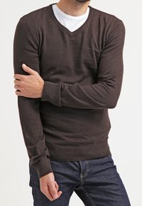 Brun v-ringad tröja gjord av mjukt tyg, med långa ärmar och ribbade muddarna och fållen. Kombinerad med mörka denimjeans.