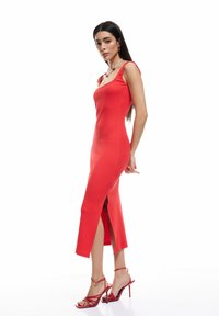 Robe rouge ajustée avec des bretelles spaghetti, fente sur le côté, texture côtelée, assortie à des talons rouges à lanières. Design simple qui met en valeur la silhouette.