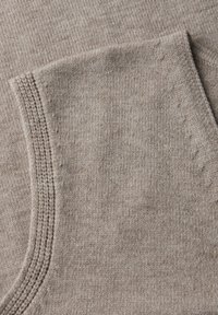Mjuk beige stickad tyg med synlig texturerad sömdetalj längs kanten, som visar en vikt hörn.