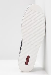 Zapatilla negra con suela de goma texturizada y fondo blanco con estrías. Presenta un logo rojo de Rieker en el lateral. Diseño minimalista sin patrones.