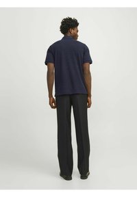 Camisa polo negra de manga corta, con tejido texturizado y cuello en contraste, combinada con pantalones rectos negros y calzado.