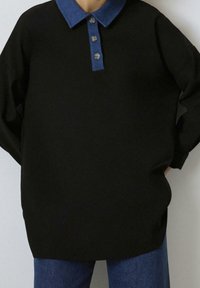 Sweatshirt noir oversize avec un col en denim, comportant trois boutons et une texture lisse, associé à un bas en denim bleu.
