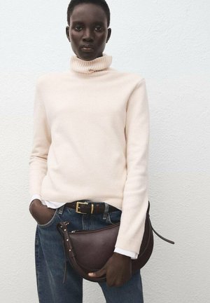 Pull à col roulé crème, jean denim bleu, sac en cuir marron. Pull en matériau doux, sac avec une forme incurvée et une fermeture éclair.