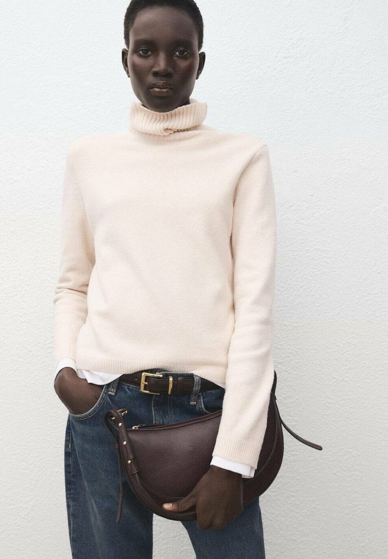 Cremfarbener Rollkragenpullover, blaue Denim-Jeans, braune Ledertasche. Pullover aus weichem Material, Tasche hat eine geschwungene Form und einen Reißverschluss.