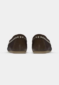Καφέ μοκασίνια από σουέντ με ομαλή υφή, στρογγυλεμένη μύτη και διακοσμητικά καρφιά κατά μήκος του πάνω μέρους. Εύκαμπτη σόλα από καουτσούκ, πίσω όψη.