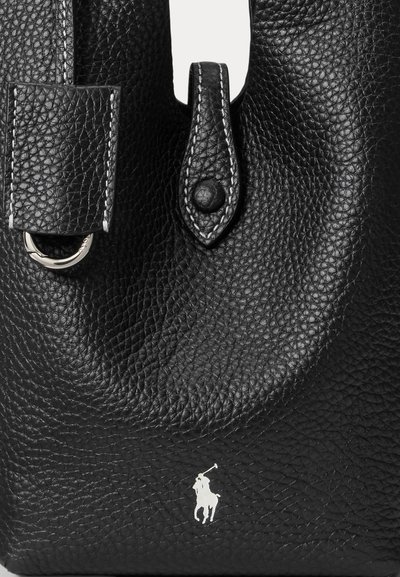 Sac en cuir noir avec une finition texturée, doté d'une fermeture à rabat proéminente et d'un logo argenté à l'avant. Les accents incluent des coutures blanches.