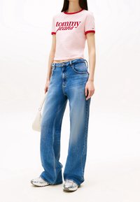 Light pink cropped t-shirt with red trim and "tommy jeans" text, paired with loose blue denim jeans and silver-accented sneakers.