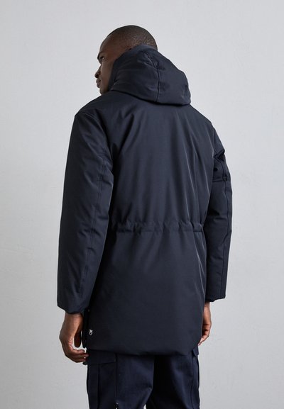 Čierna, vypchávaná parka s kapucňou, so sťahovacím pásom, dlhými rukávmi a logom blízko lemu. Mäkka textúra.