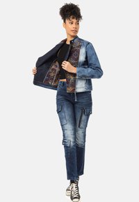 Jeansjacke mit gemustertem Innenfutter, kombiniert mit strukturierten Cargo-Jeans. Beide Teile weisen eine Mischung aus hellen und dunklen Blautönen auf.