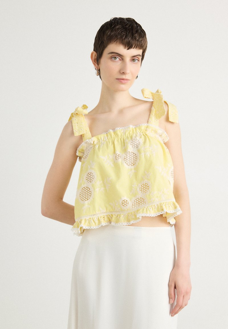 Top court jaune avec un ourlet à volants, broderies florales et découpes circulaires. Les bretelles réglables et la dentelle mettent en valeur le design.