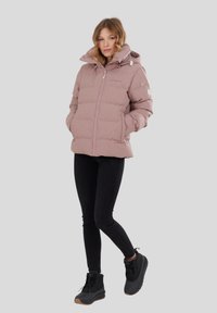 Giacca a vento rosa con cappuccio, dotata di chiusura a zip e tasche laterali. Abbinata a jeans neri e stivali neri con suole marroni.