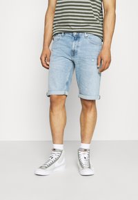 Svetle modré džíny šortky s ohrnutými lemy, spárované se šedým a bílým pruhovaným tričkem a šedými teniskami na vysoké podrážce.