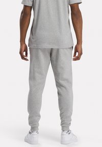 Grijze sweatpants met een ontspannen pasvorm, elastische boorden en een zachte textuur, gecombineerd met witte sneakers met zwarte en rode accenten.