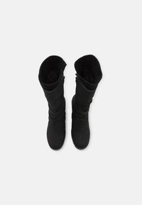 Bottes noires montantes jusqu'aux genoux avec une semelle en caoutchouc souple, présentant un design décontracté et un manchon supérieur en tricot côtelé. Texture lisse dans l'ensemble, sans éléments métalliques visibles.
