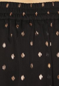 Svart tyg med elastisk midjeband och metalliska guldprickar med en texturerad yta, som visar ett växlande mönster.