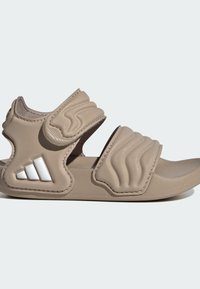 Sandalia beige con punta abierta, dos tiras de velcro acolchadas y un logo triangular blanco en la correa del talón.