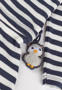 Gestreifter Stoff in Marineblau und Weiß mit einem kleinen grauen Tags in Eulenform, der einen orangefarbenen Schnabel und Füße hat und zwischen zwei Abschnitten befestigt ist.