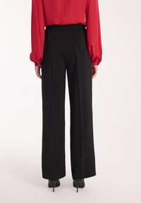 Czarne spodnie szerokie z elastycznym pasem, gładka tekstura, w połączeniu z czerwonym bluzką z długim rękawem, widoczne eleganckie czarne szpilki.