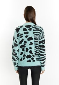 Fluffy trui in lichtblauw met zwart dierenprintmotieven, met zowel luipaardvlekken als zebrapatronen over de rug.