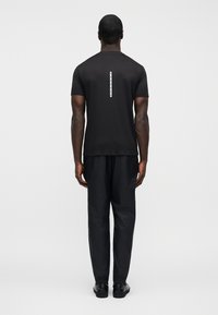 Μαύρο κοντομάνικο μπλ ουζάκι με κάθετη ανακλαστική λεπτομέρεια στην πλάτη, συνδυασμένο με μαύρο υφασμάτινο παντελόνι και μαύρα παπούτσια.