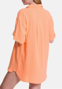 Kurzärmliges, kragenloses Hemd in hellem Orange, aus strukturiertem Stoff gefertigt. Verfügt über einen Rückenfalten und hochgerollte Ärmel sowie einen lässigen Schnitt.