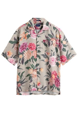 Chemise beige à manches courtes avec des motifs floraux larges en rose, rouge, orange et blanc, accompagnés de feuilles vertes, dotée d'une poche poitrine.