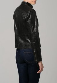 Giubbotto di pelle nera con design aderente, finitura texture, colletto alto e polsini con zip. Le maniche presentano cuciture dettagliate.