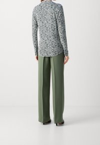 Langarmshirt in een groen-wit abstract patroon, gecombineerd met hoge, wijde groene broek en zwarte hakken.
