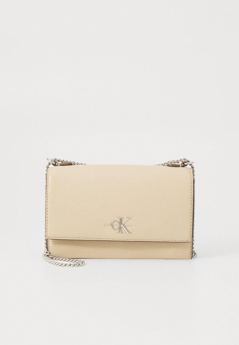 Krämfärgad läderclutch med en vikbar design, silverkedjeslinga och präglad CK-logotyp på framsidan. Slät textur och minimalistisk stil.