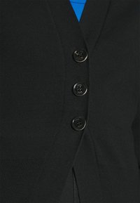 Gros plan d'un cardigan noir avec trois boutons noirs brillants sur une chemise bleue.