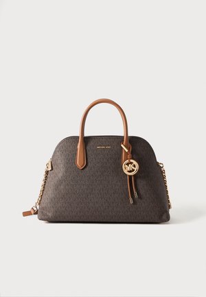 Sac à main Michael Kors marron avec des anses couleur cognac, une bandoulière en chaîne dorée, et un pendentif rond doré avec le logo MK sur un fond clair uni.