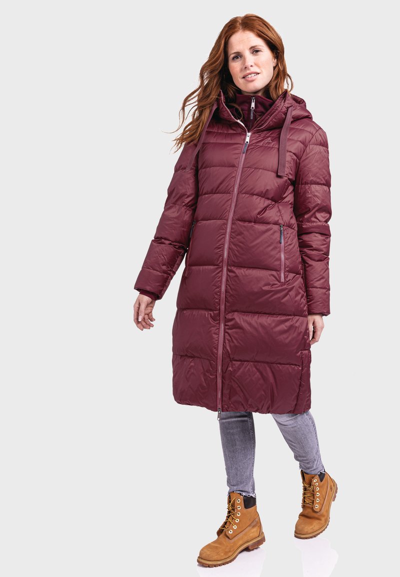 Maronfarbener Puffermantel mit Reißverschluss vorne, Kapuze und zwei seitlichen Reißverschlusstaschen. Kombiniert mit grauen Jeans und hellbraunen Schnürstiefeln.