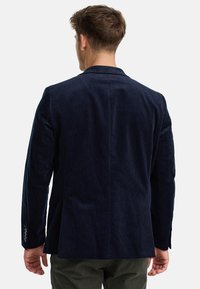 Blazer en velours côtelé bleu marine avec un col cranté, une fente au dos et des poignets boutonnés. Le tissu a une texture douce et côtelée.