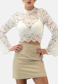 Witte kanten cropped top met lange, uitlopende mouwen en een geschulpte zoom, gecombineerd met een beige minirok met een voorzak en een gestructureerde stof.