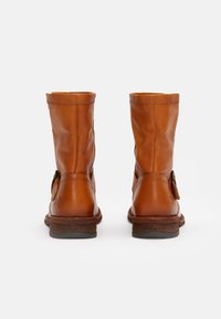 Braune Leder-Stiefeletten mit einem lässigen Design, ausgestattet mit einer seitlichen Schnalle und einem Holzabsatz. Glatte Textur mit einem leichten Glanz.
