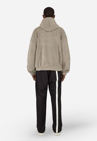 Túlméretezett, kapucnis szürke polárdzseki strukturált felülettel. Fekete nadrággal párosítva, amelynek fehér oldalsávja van. Minimalista dizájn.