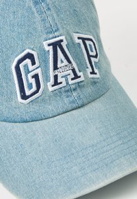 Világoskék farmer baseball sapka, amelyen hímzett "GAP" logó található sötétkékkel. A sapka ívelt szélekkel és varrott részletekkel rendelkezik.