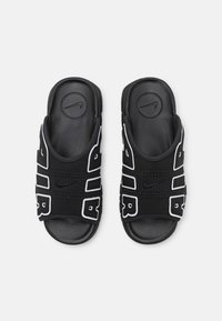Sandale negre cu accente albe, având o talpă texturată, curele perforate și un logo circular Nike în partea de sus.