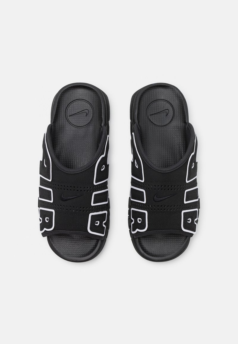 Chanclas negras con detalles blancos, con una plantilla texturizada, correas perforadas y un logo circular de Nike en la parte superior.