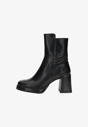 Botte en cuir noire mi-mollet avec talon bloc, bout carré, coutures latérales discrètes et logo embossé près de la cheville sur un fond blanc.