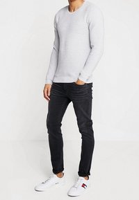 Pull à manches longues rayé gris clair avec un col rond, associé à un jean noir slim et des baskets blanches avec des accents colorés.