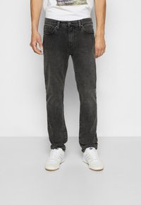 Svarte denimjeans med rett snitt, med fem lommer og en subtil slitt tekstur, sammen med hvite joggesko.